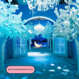Glowing blue enchanted forest installation with white blossom trees and crystal chandeliers at House of Dreamers London