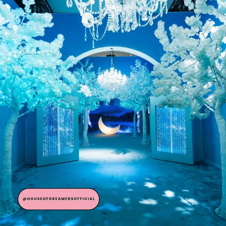 Glowing blue enchanted forest installation with white blossom trees and crystal chandeliers at House of Dreamers London