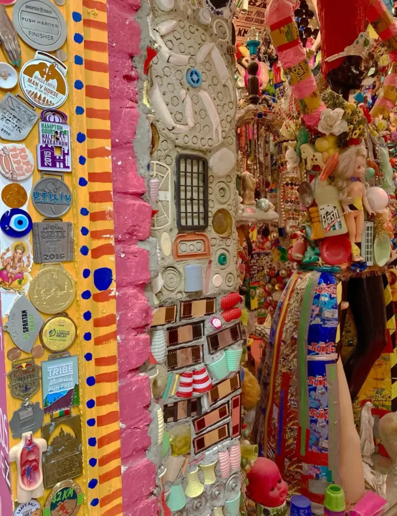 Wall of race medals beside a mosaic pillar studded with pottery and plastic trinkets at House of Dreams, East Dulwich