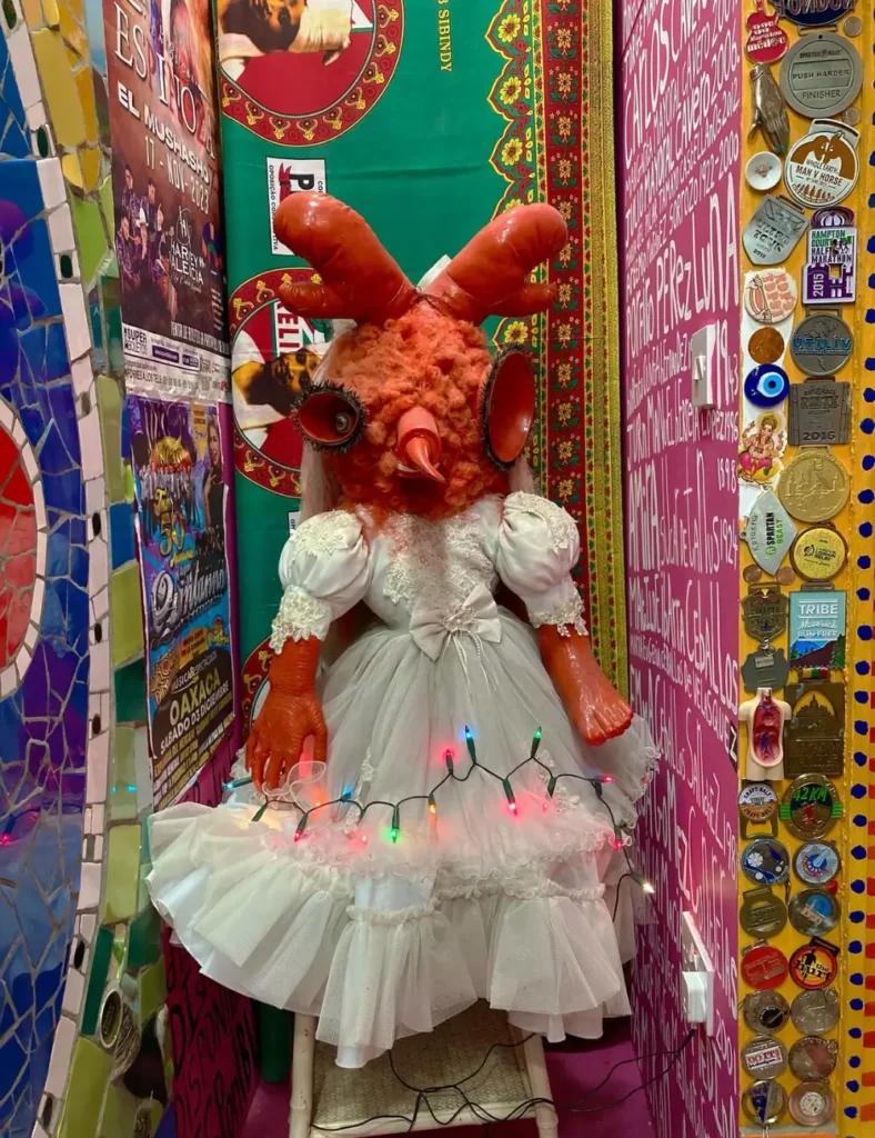 Horned orange figure in a frilly white dress and fairy lights against a pink wall at House of Dreams, East Dulwich