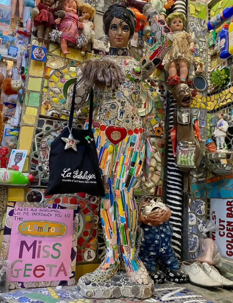 Mosaic figure covered in pens and pottery beside a โGlamorous Miss Geetaโ sign at House of Dreams Museum, East Dulwich
